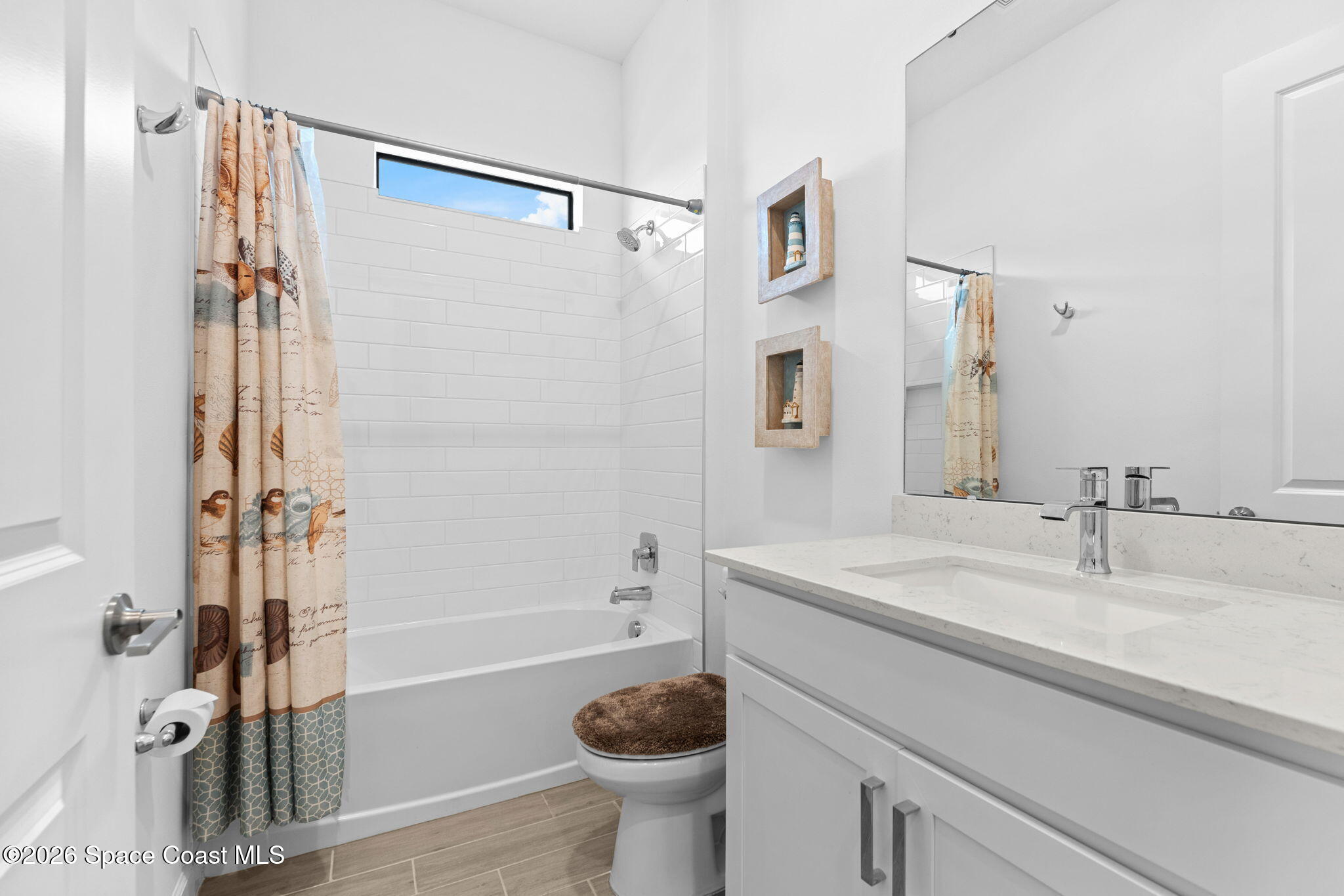 Bright bathroom with a white subway-tile tub surround, patterned shower curtain, and wide white vanity.