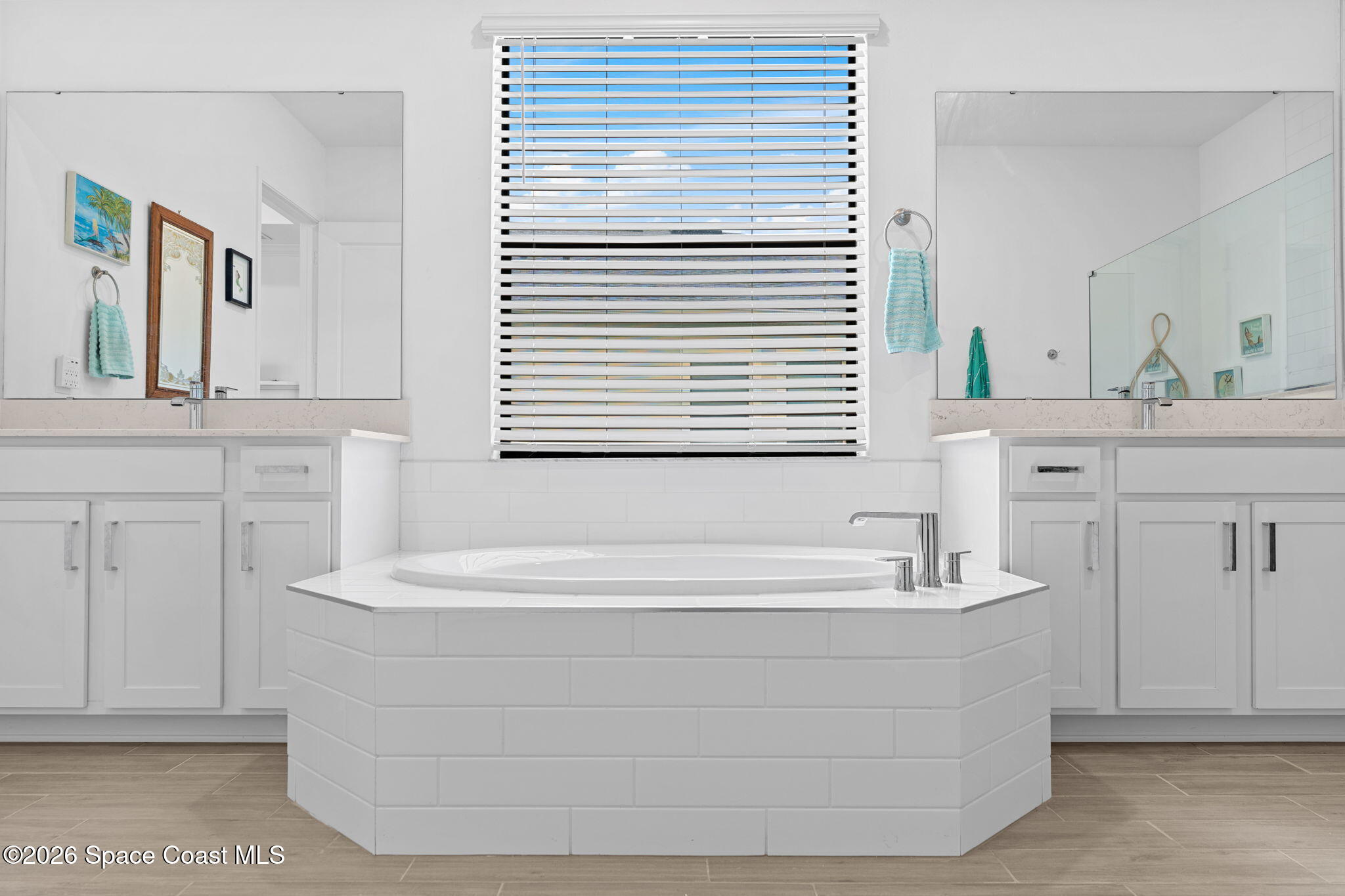 Bathroom with a built-in soaking tub between dual vanities and a window with blinds.