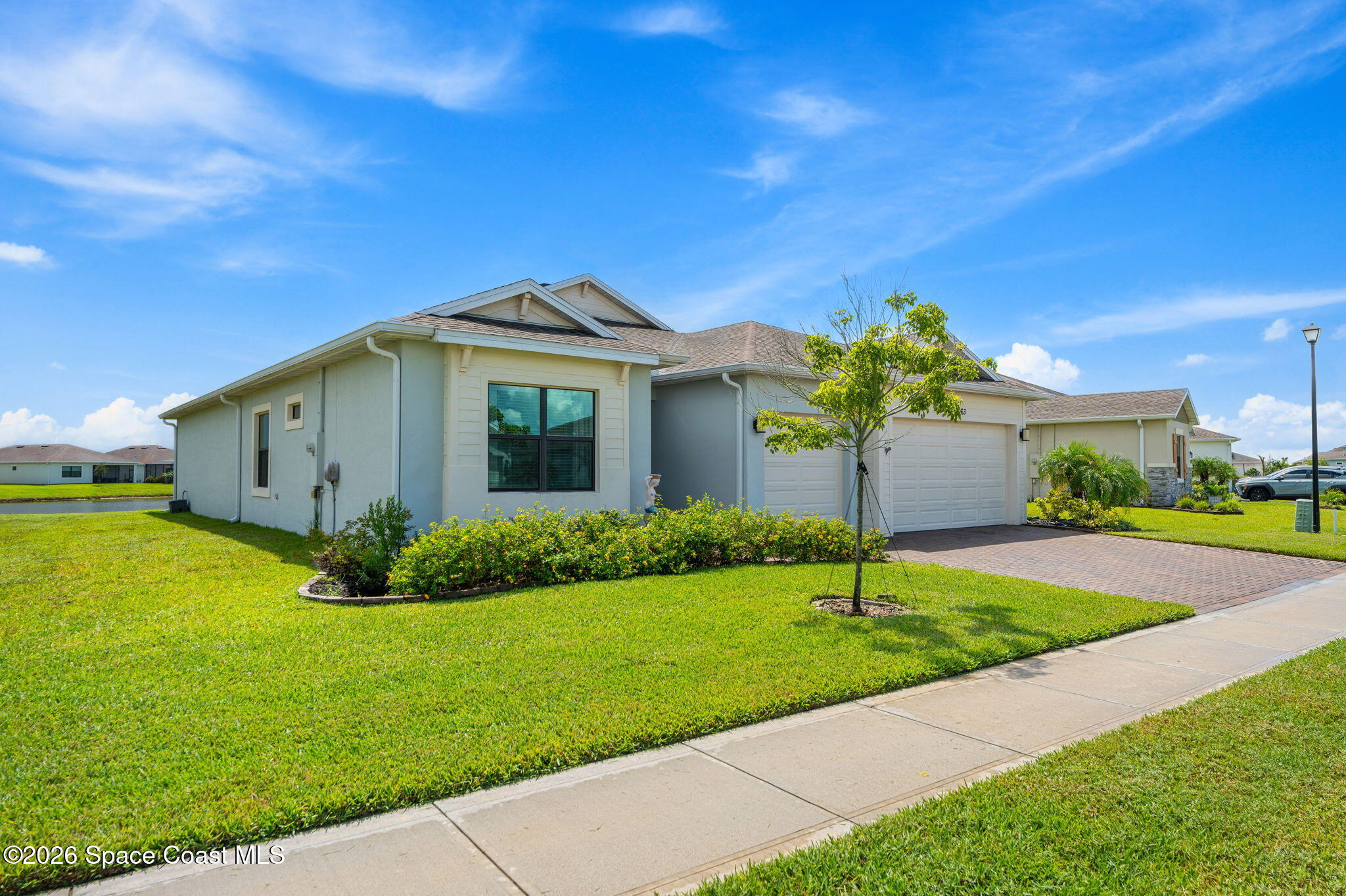 Single-story home with a two-car garage, brick-paver driveway, and landscaped lawn.