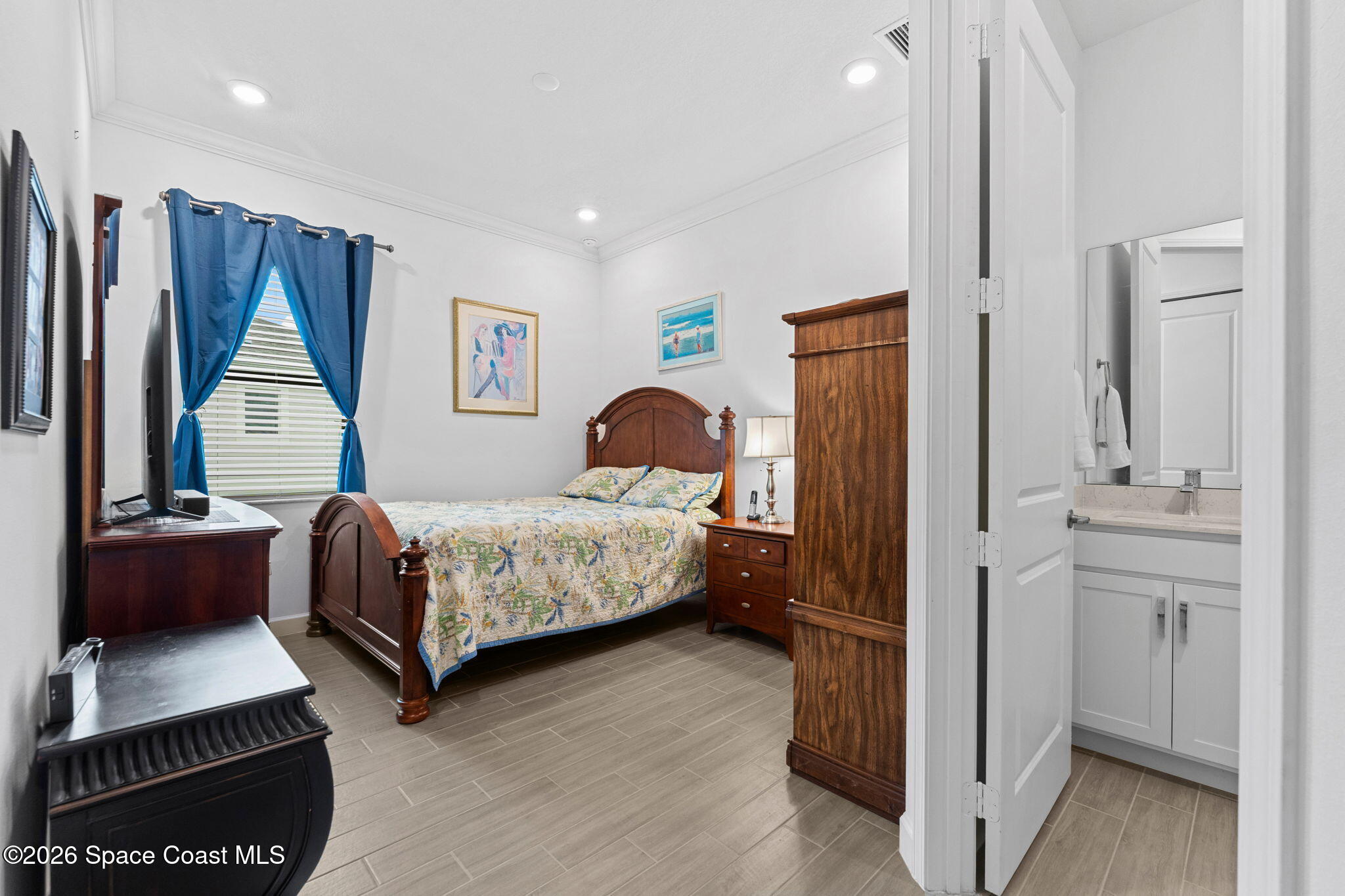 Furnished bedroom with a wooden bed and blue curtains, opening to an adjoining bathroom.
