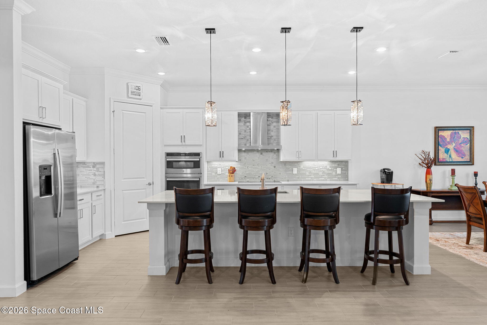 Kitchen with a large island, four bar stools, white cabinets, and stainless steel appliances.