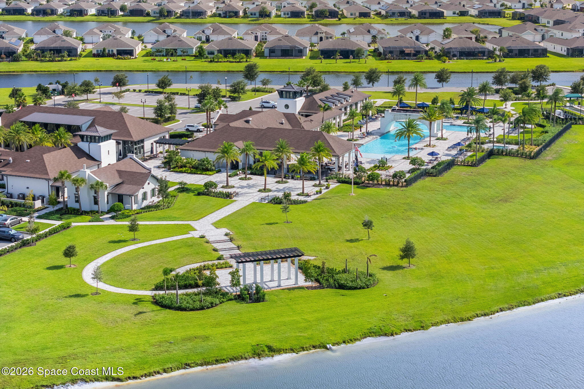 Aerial view of a community clubhouse and swimming pool beside a canal and landscaped lawn.