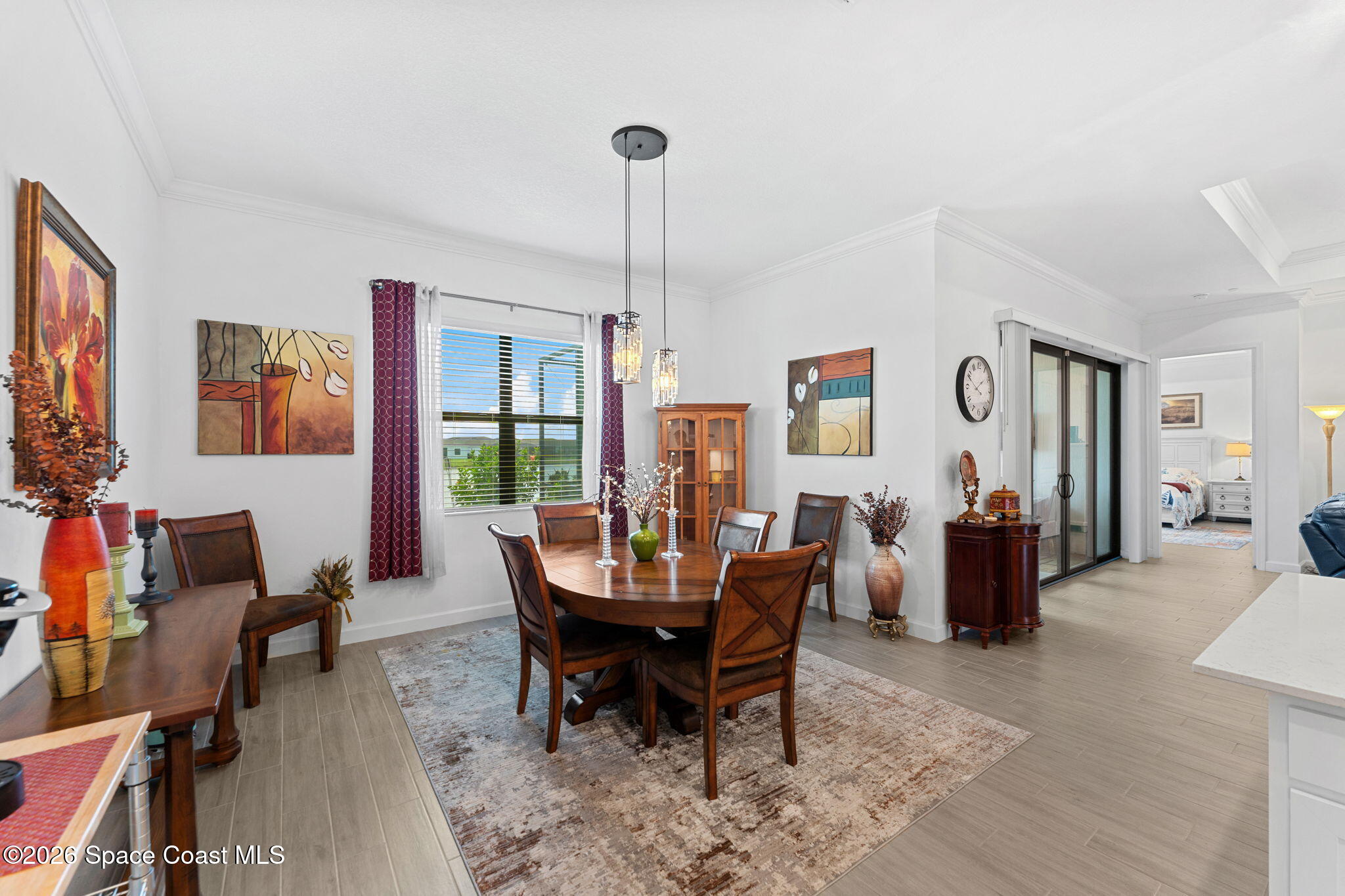 Dining room with a round wooden table, patterned rug, and burgundy curtains beside a bright window.