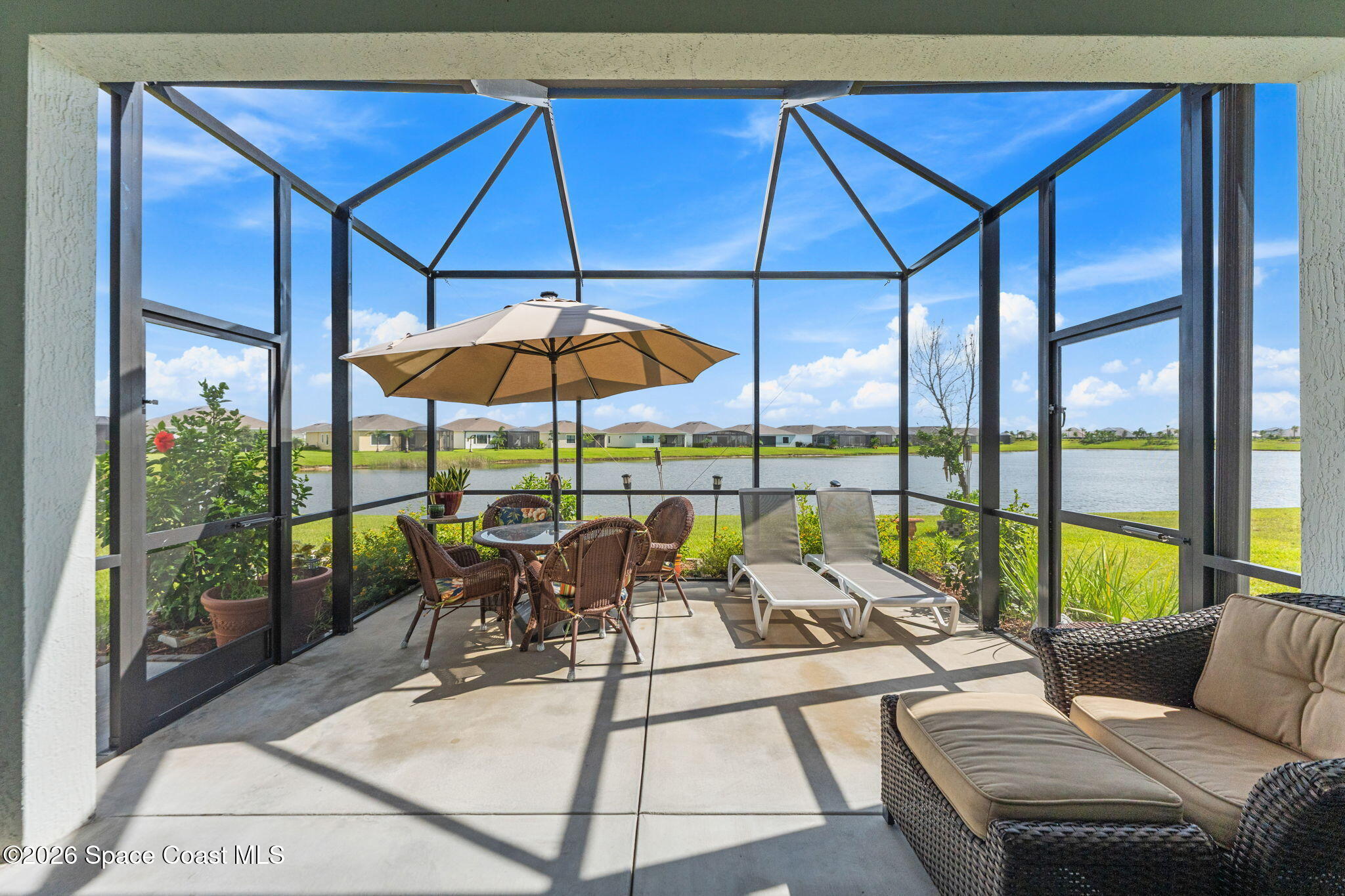 Screened patio with wicker seating and lounge chairs overlooking a lake.