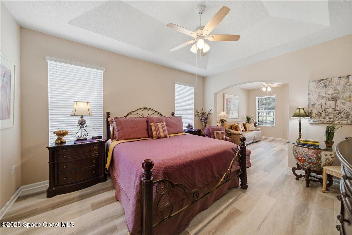 Primary bedroom with burgundy bed, tray ceiling, and arched opening to a sitting area.
