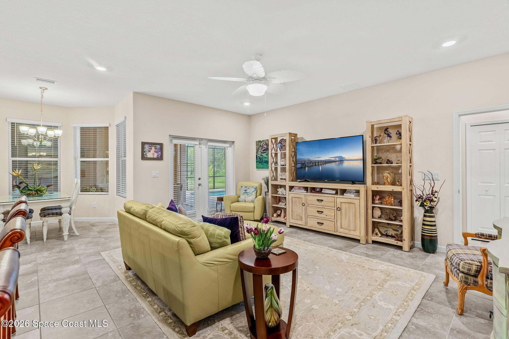 Living room with pale yellow seating, tiled floors, and a large TV on a light wood entertainment center.