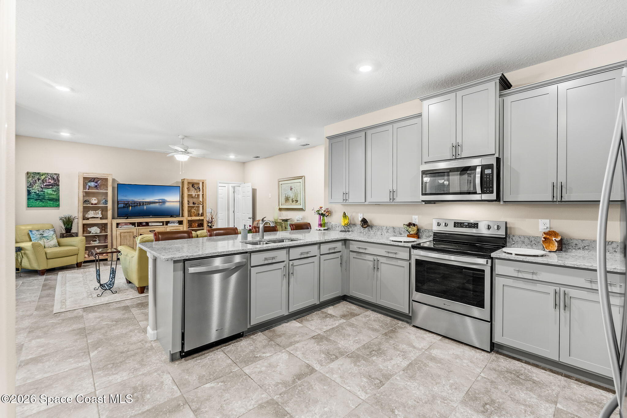 Kitchen with gray cabinetry, stone island, stainless steel appliances, and an adjoining living area.