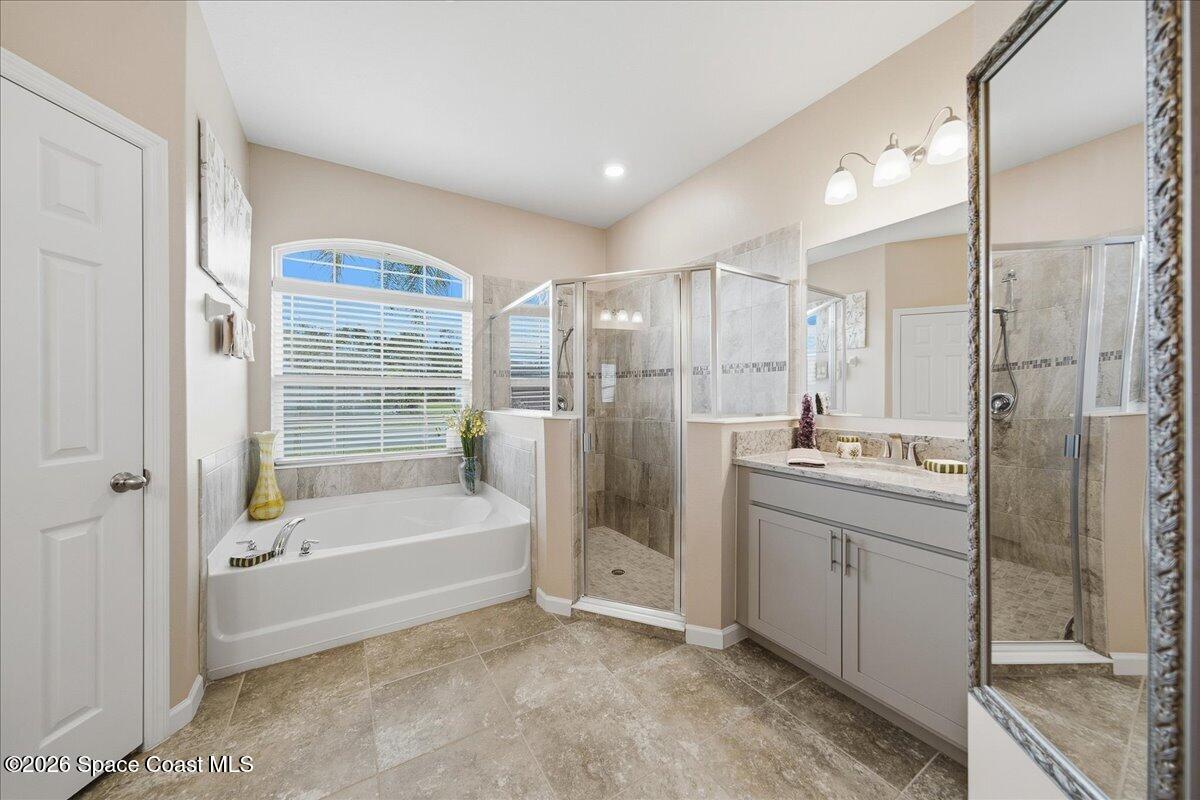 Primary bathroom with a soaking tub beneath an arched window and a glass-enclosed tiled shower.