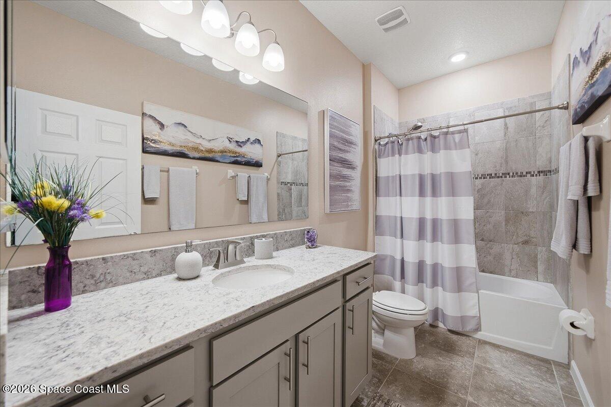 Bathroom with a long gray vanity and marble-look counter beside a tiled tub with striped shower curtain.