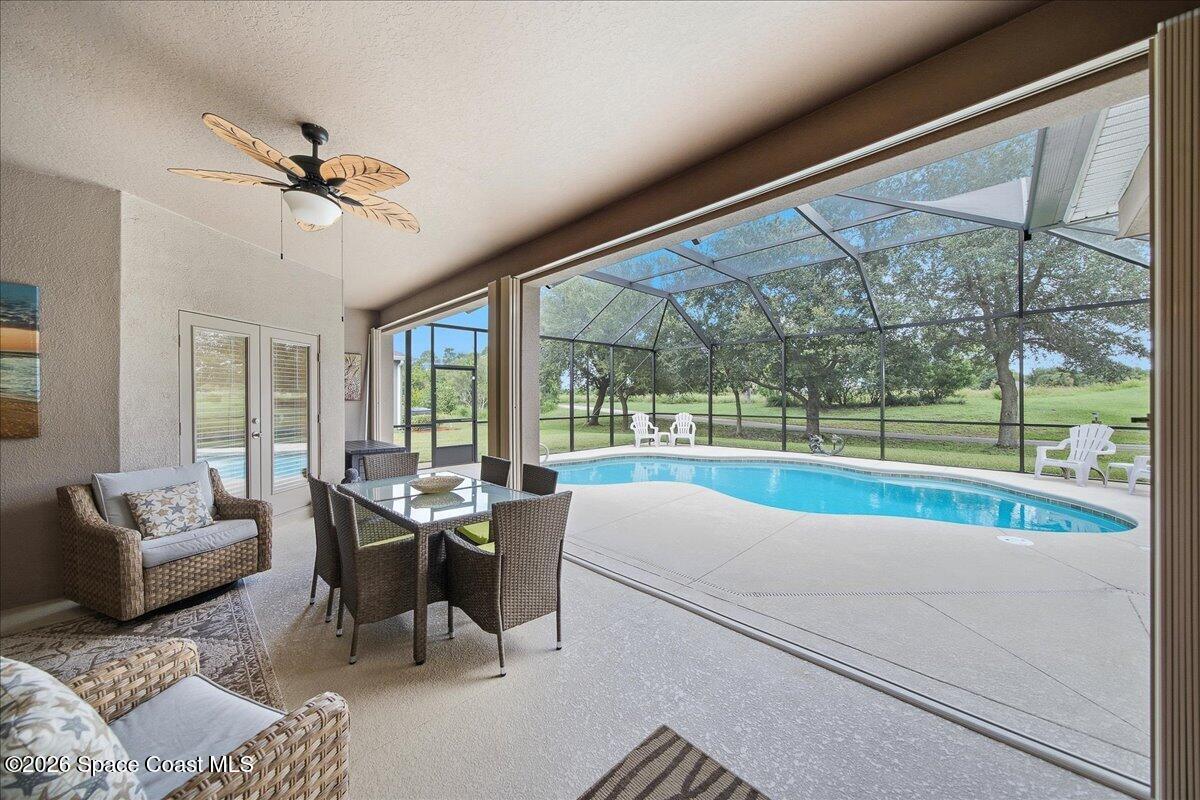 Covered patio with wicker seating and dining table beside a screened swimming pool.