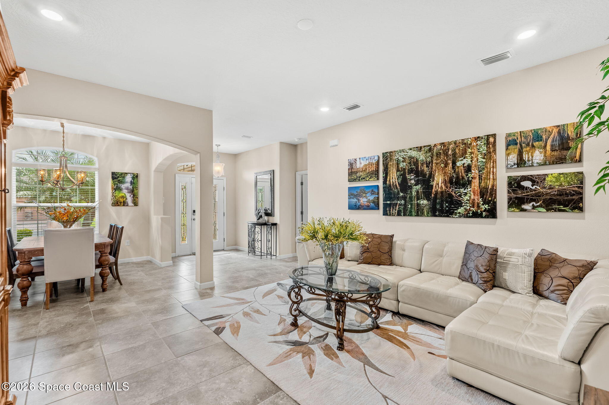 Living room with a cream sectional, glass coffee table, and adjoining dining area beside a large window.