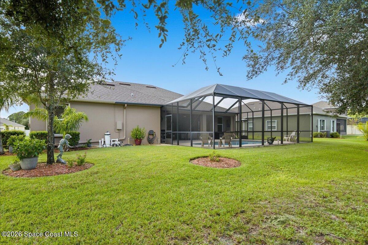 Rear of beige home with screened pool enclosure, patio seating, and green lawn.