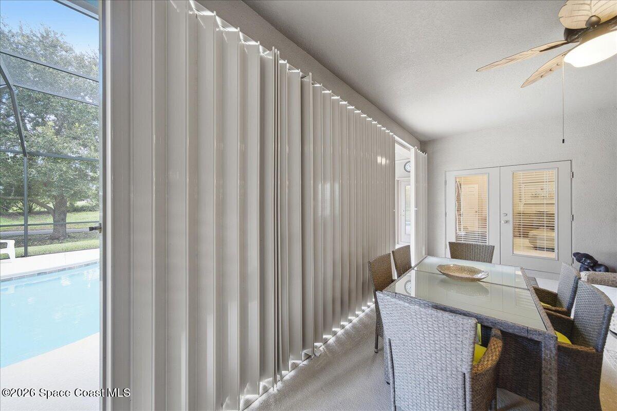 Enclosed dining area with a glass-top wicker table and views of the pool through vertical blinds.