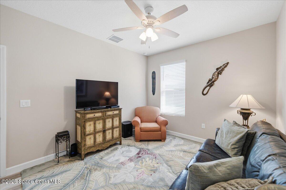 Living room with a leather sofa, peach armchair, television cabinet, ceiling fan, and patterned rug.