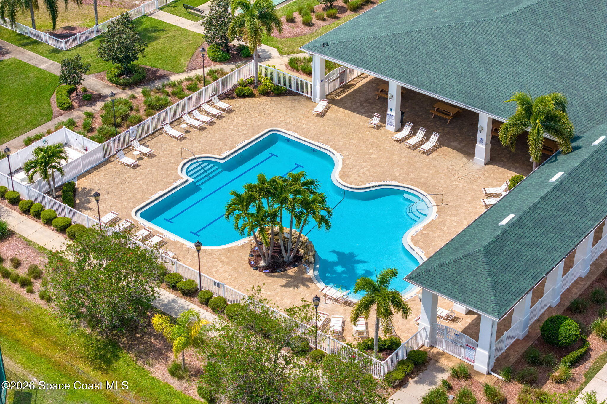 Outdoor pool with a palm island, lounge chairs, and a covered pavilion, viewed from above.