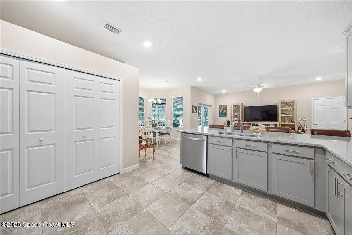 Kitchen with gray cabinetry, a long stone island, tile floors, and adjoining dining and living areas.