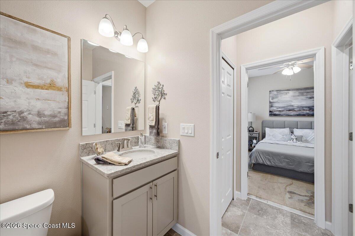 Bathroom vanity with stone countertop and mirror, looking through a doorway into a bedroom.