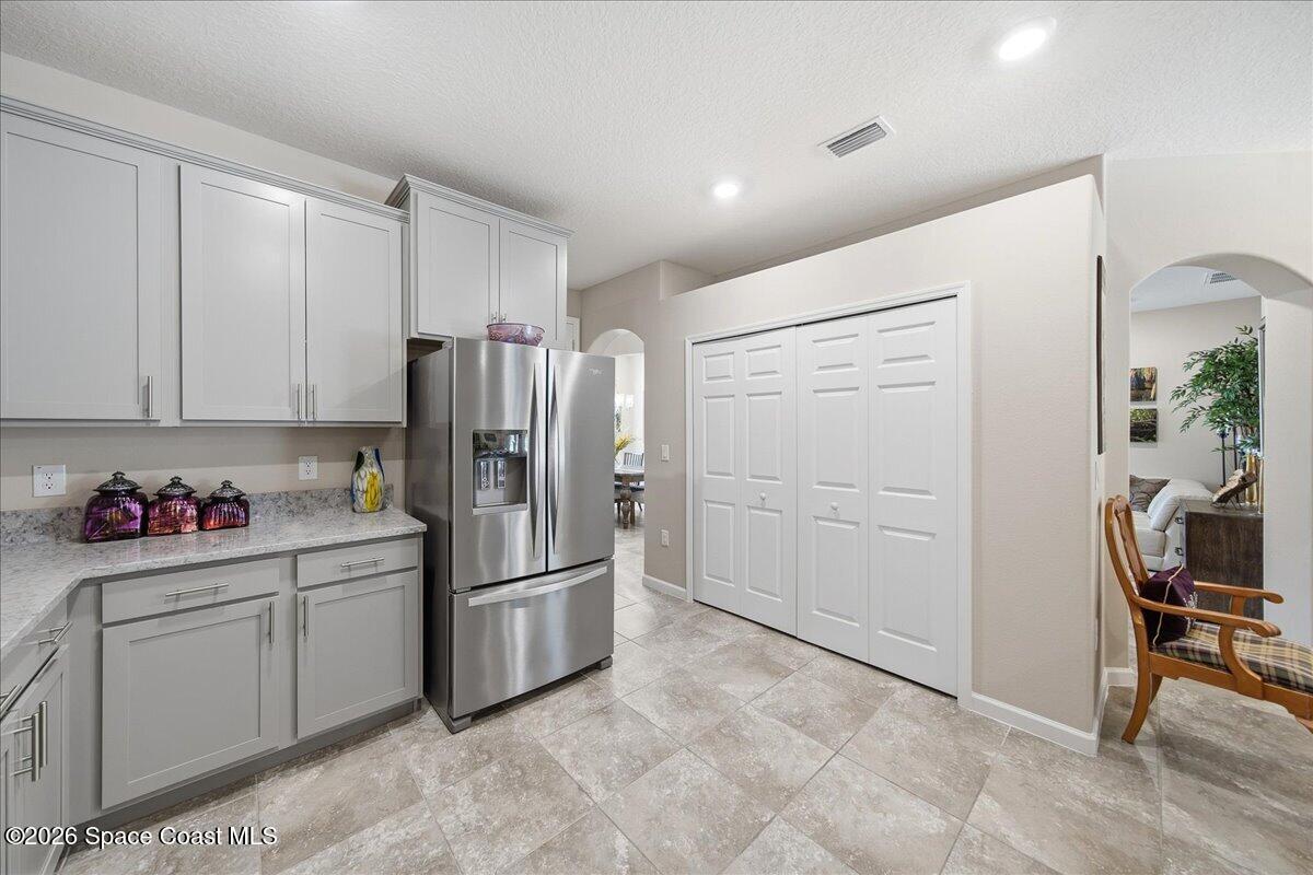 Kitchen with white cabinetry, stainless-steel refrigerator, and an arched opening to the living area.