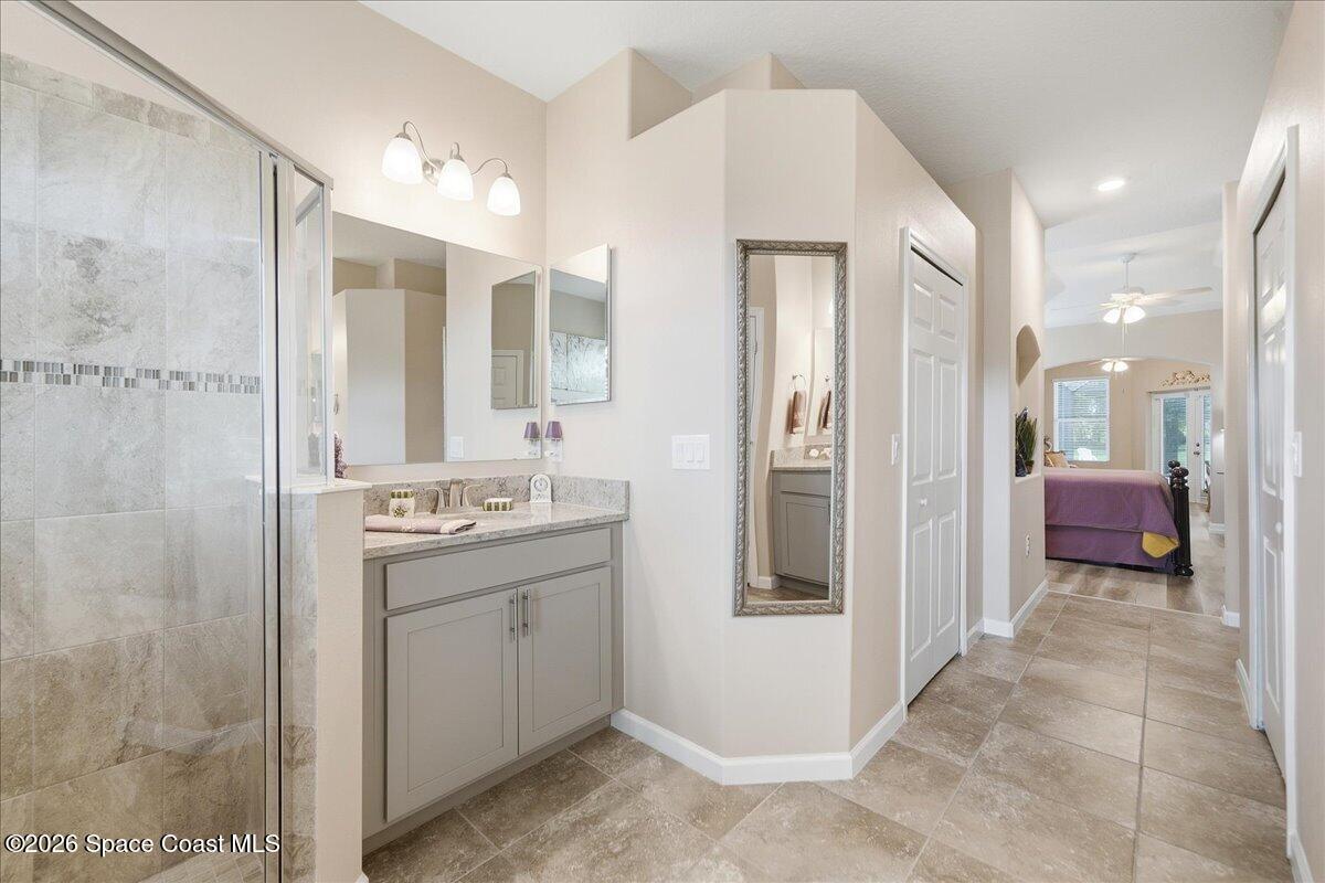 Bathroom with a glass shower and gray vanity, opening onto a hallway and bedroom.