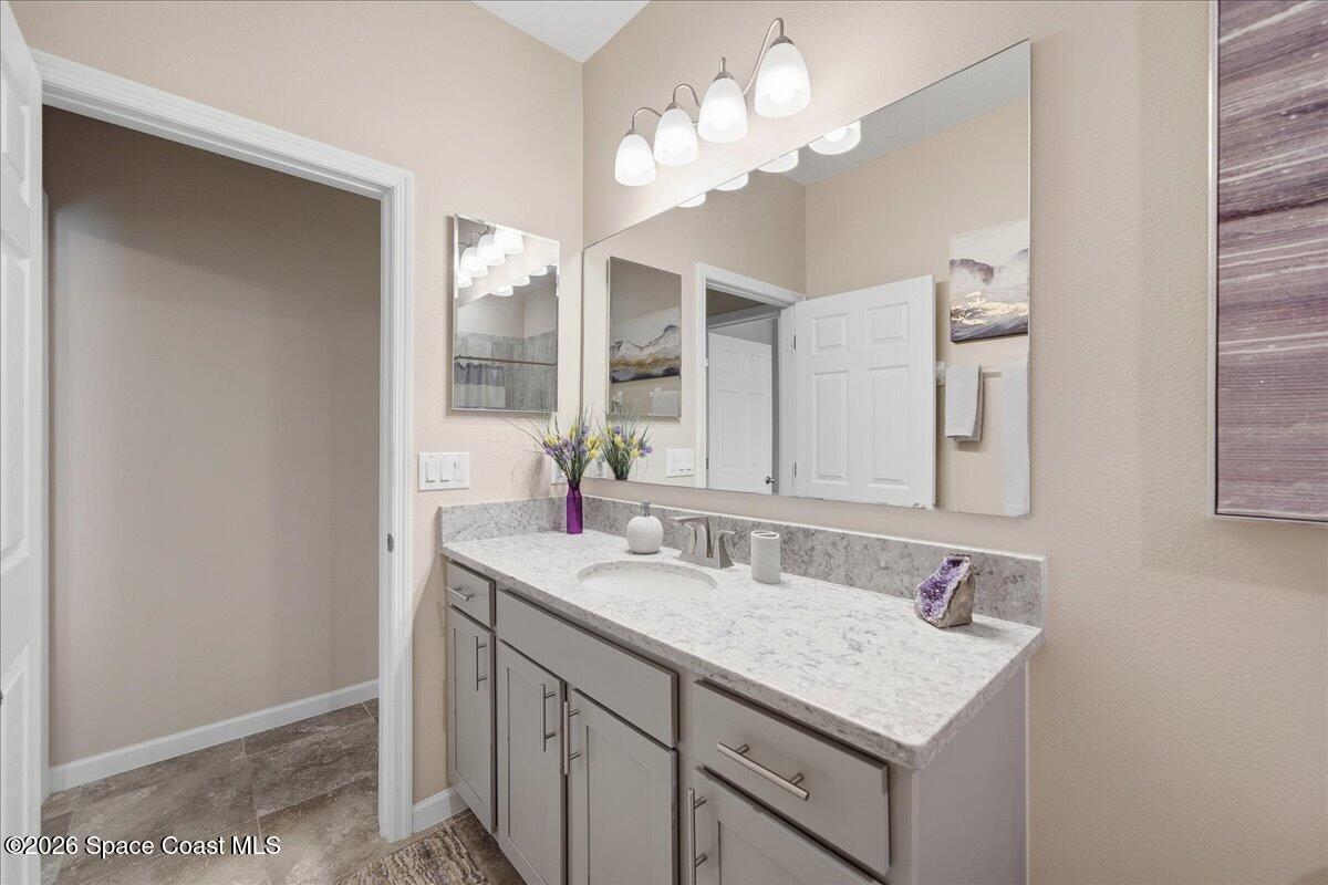 Bathroom vanity with gray cabinets, a stone countertop, and a large mirror.