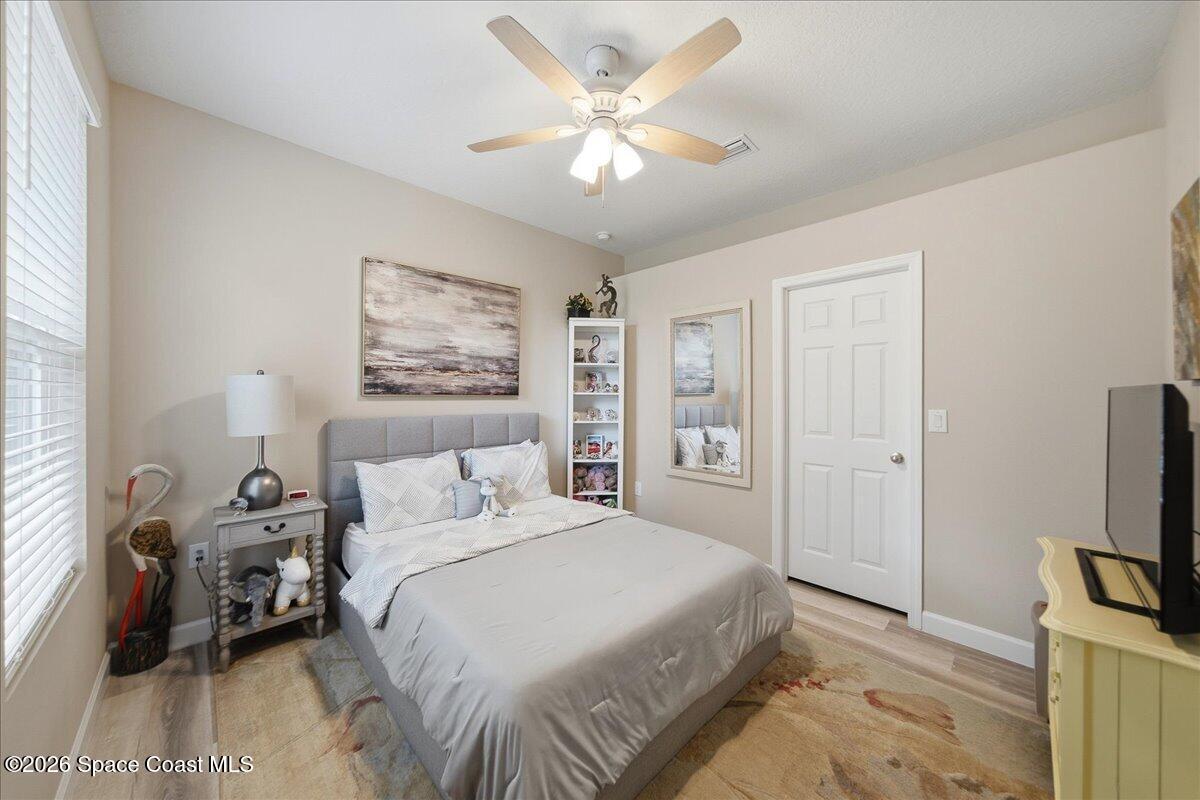 Furnished bedroom with a gray upholstered bed, white bedding, and a ceiling fan.