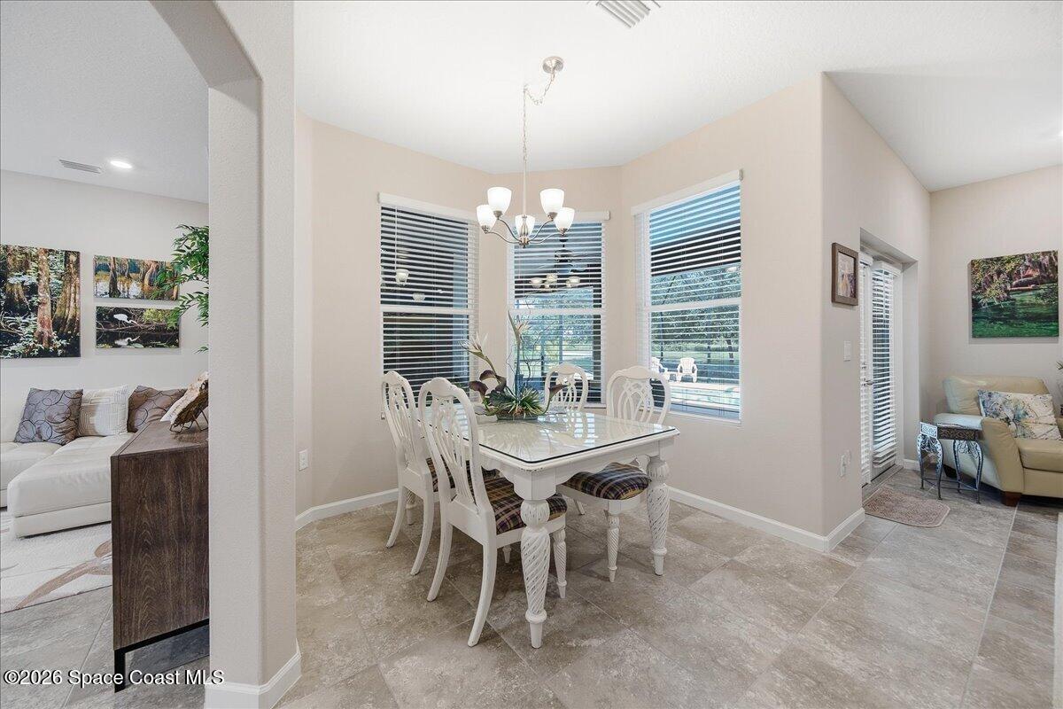 Dining room with a white glass-top table, chandelier, and windows overlooking a pool.