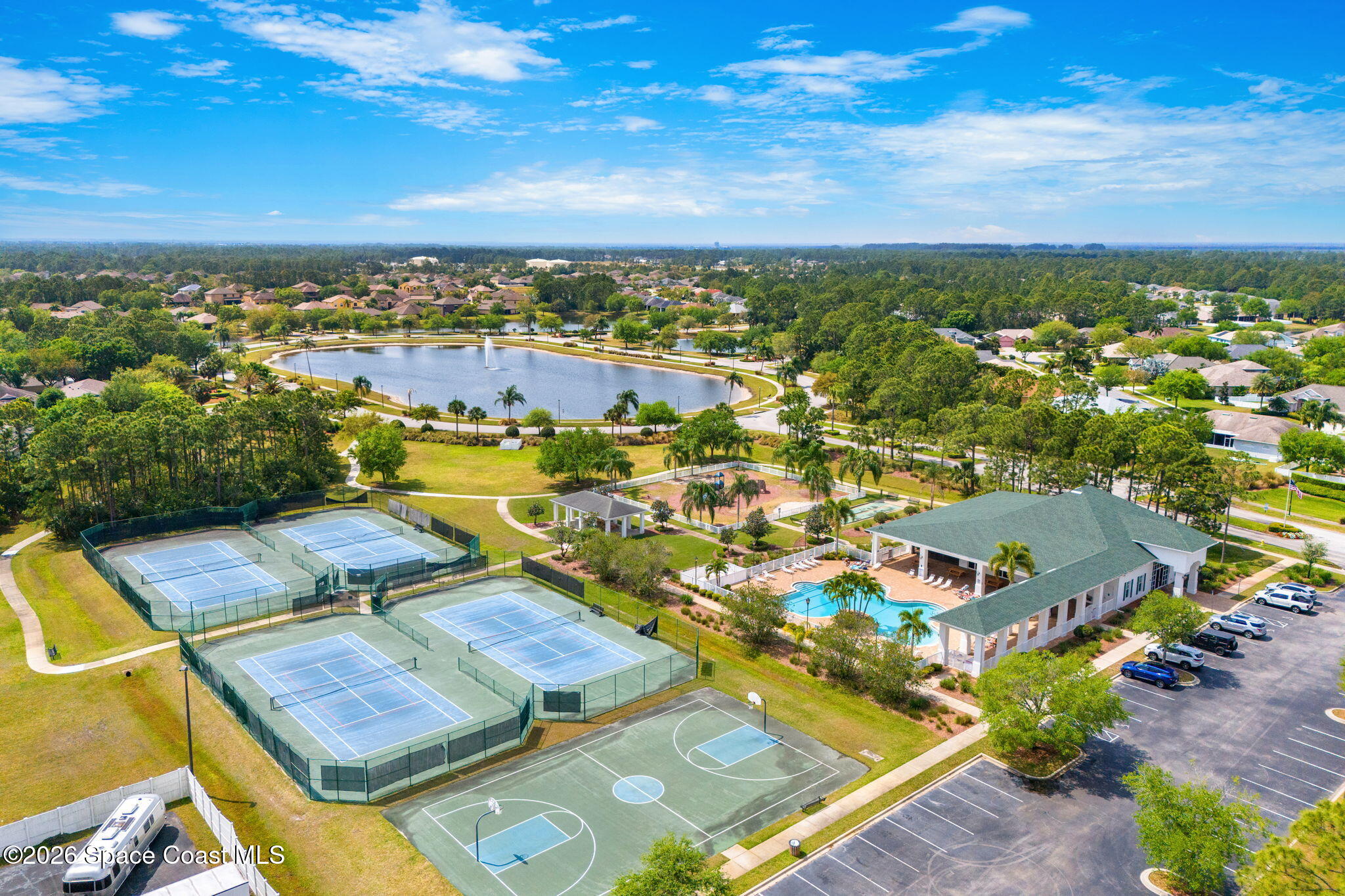 Aerial view of community amenities with tennis courts, a pool, clubhouse, and fountain lake.