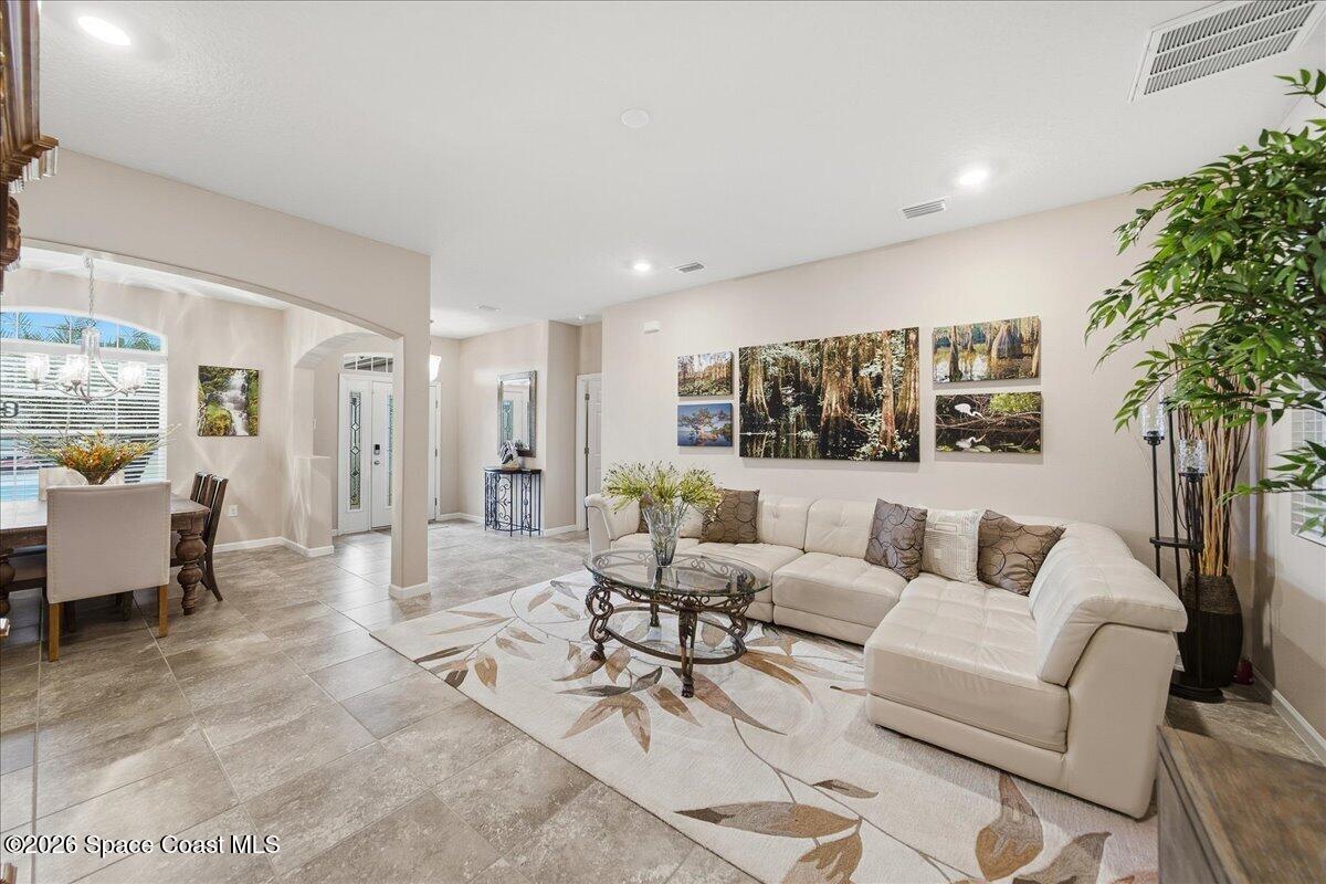 Living room with a white sectional, patterned rug, and nature artwork; dining area visible beyond.