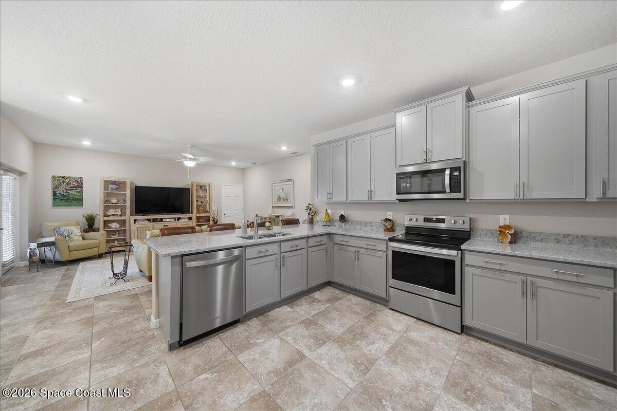 Kitchen with a large island, gray cabinetry, stainless steel appliances, and an adjoining living area.