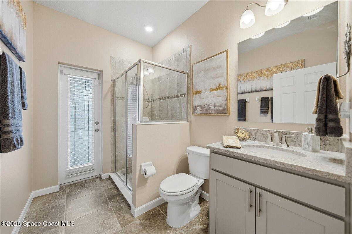 Bathroom with a glass shower, gray vanity, stone countertop, and windowed door.