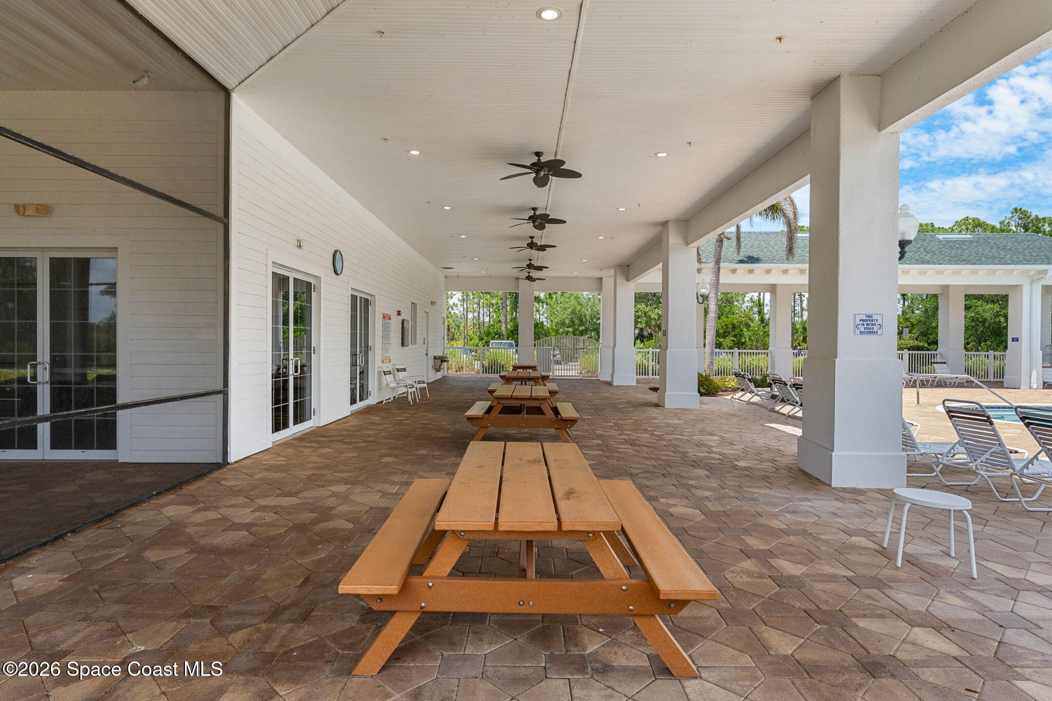Covered community patio with wooden picnic tables and ceiling fans beside a pool.