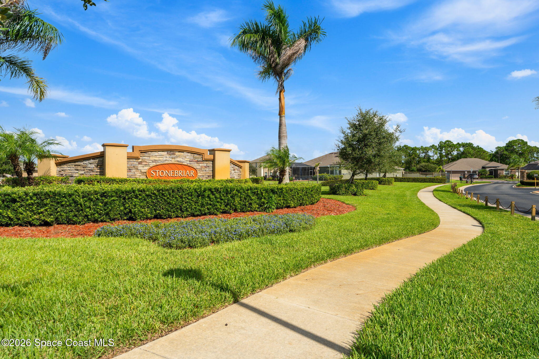 Stonebriar community entrance sign amid palm trees and landscaped lawns beside a curving sidewalk.