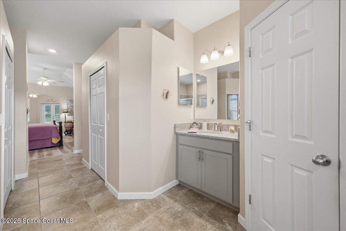 Bathroom vanity with gray cabinetry and twin mirrors beside a tiled hallway leading to a bedroom.