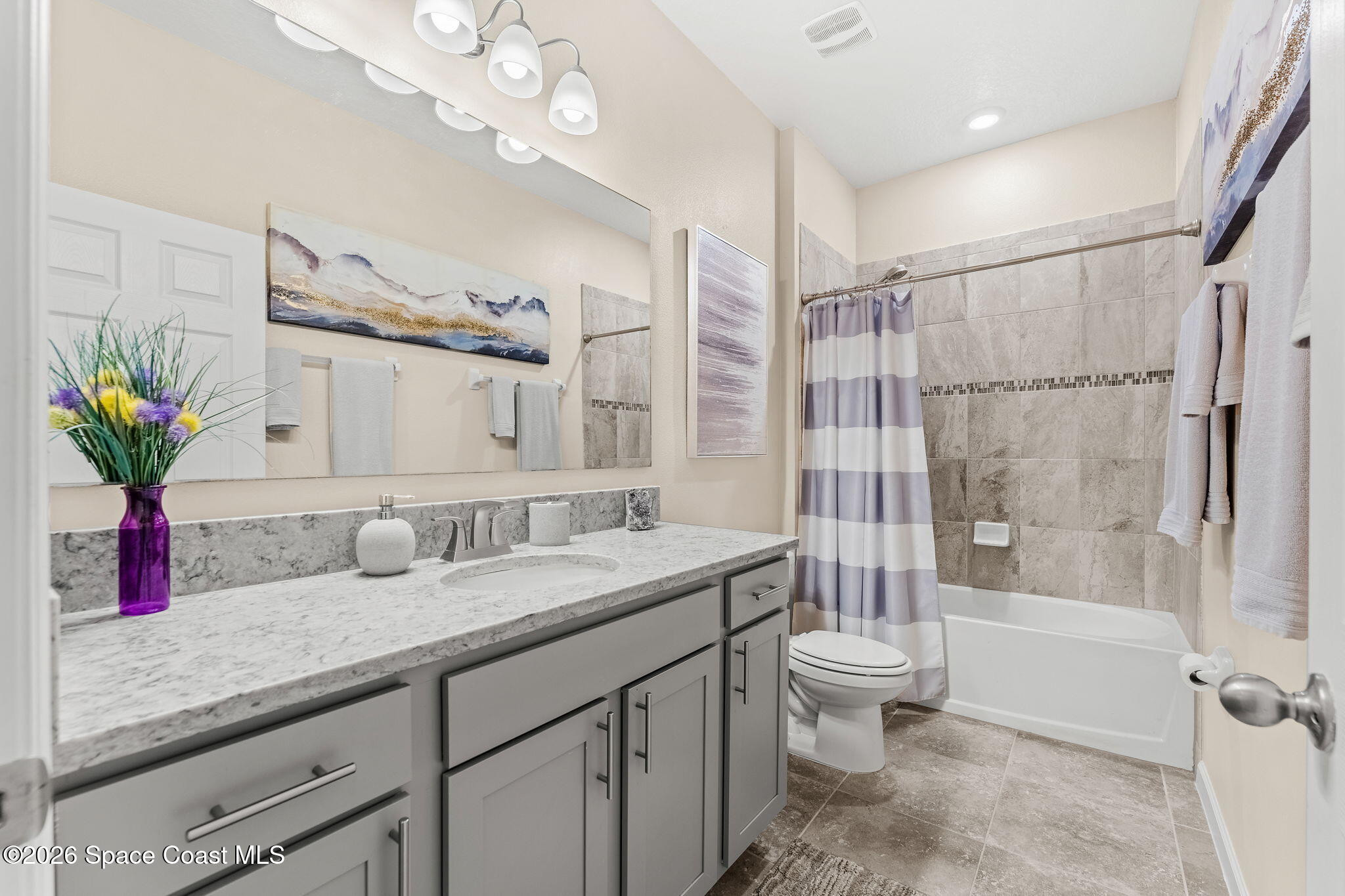 Bathroom with a gray vanity, stone countertop, and tiled tub and shower with a striped curtain.