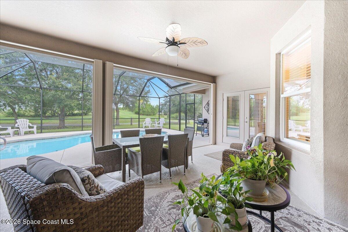 Screened lanai with wicker seating and plants overlooking a swimming pool.