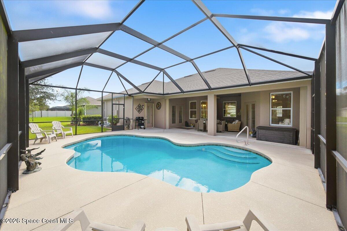 Backyard pool beneath a screened enclosure, with a curved shape, pale patio, and seating.