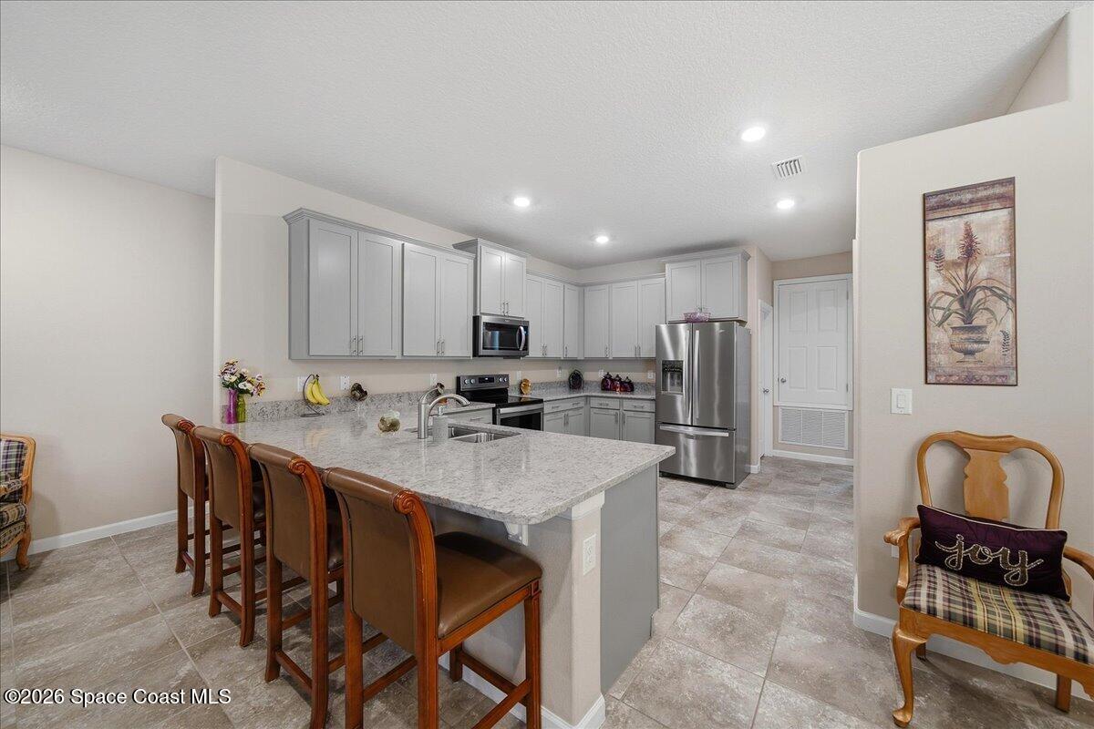 Kitchen with gray cabinets, stainless steel appliances, granite island, and wooden bar stools.