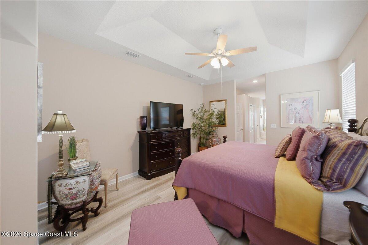 Bedroom with a tray ceiling, ceiling fan, and purple bed facing a television.