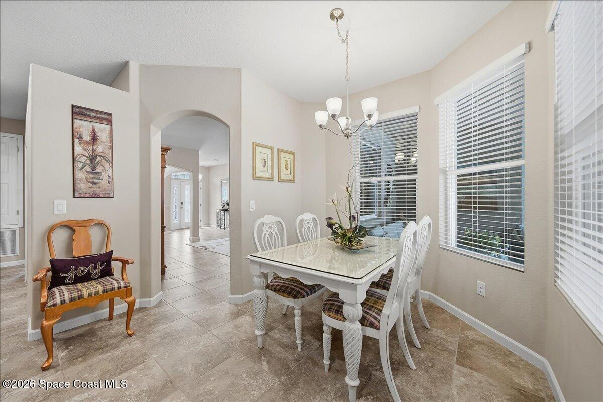 Dining room with a white table and chairs, chandelier, large windows, and tiled floors.