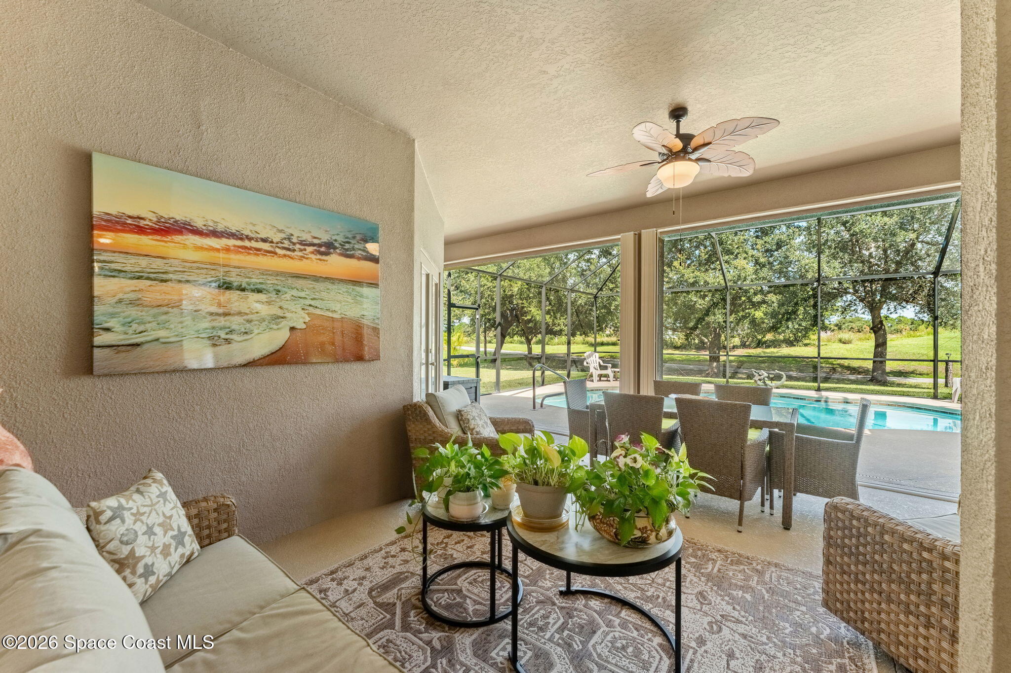 Furnished sunroom with potted plants and wicker seating overlooking a screened swimming pool.