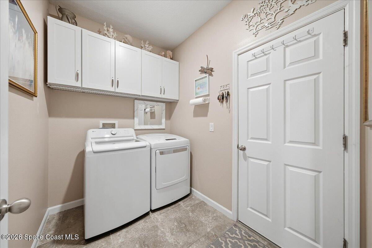 Laundry room with white washer and dryer beneath wall cabinets beside a paneled door.