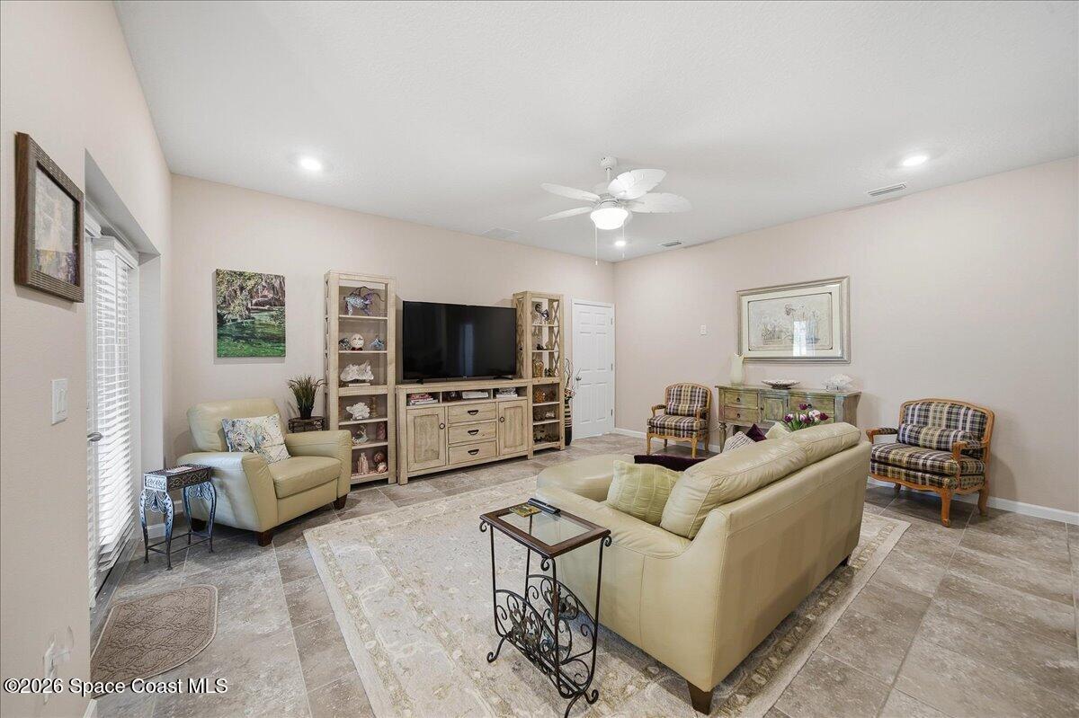 Furnished living room with beige leather seating, a large television, plaid armchairs, and tiled floors.
