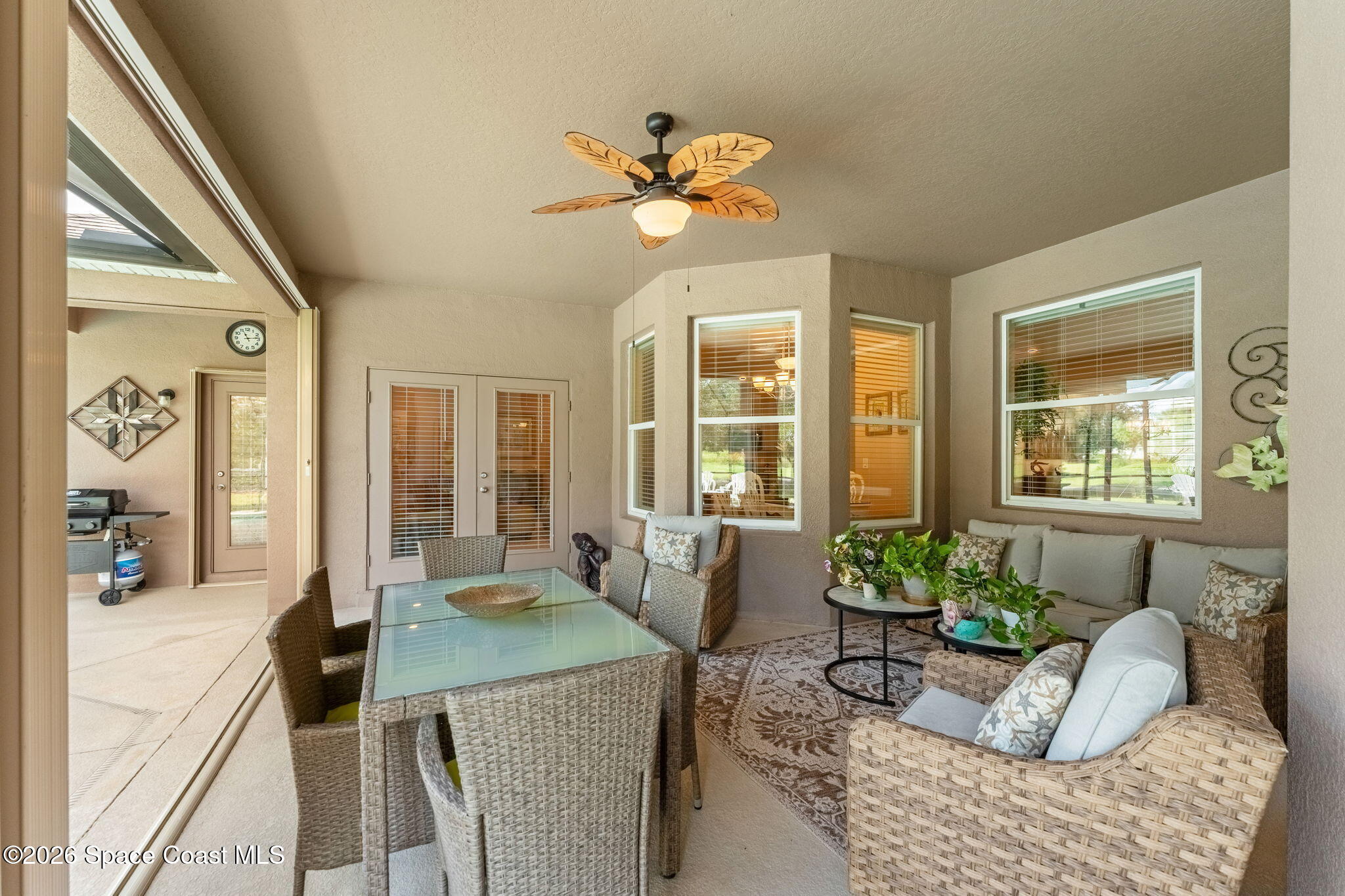 Furnished covered patio with wicker seating, a glass-top dining table, and a leaf-shaped ceiling fan.