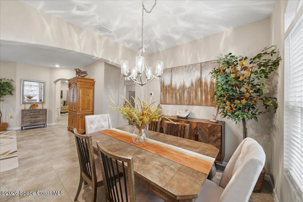 Dining room with a long wooden table, chandelier, abstract wall art, and tile flooring.