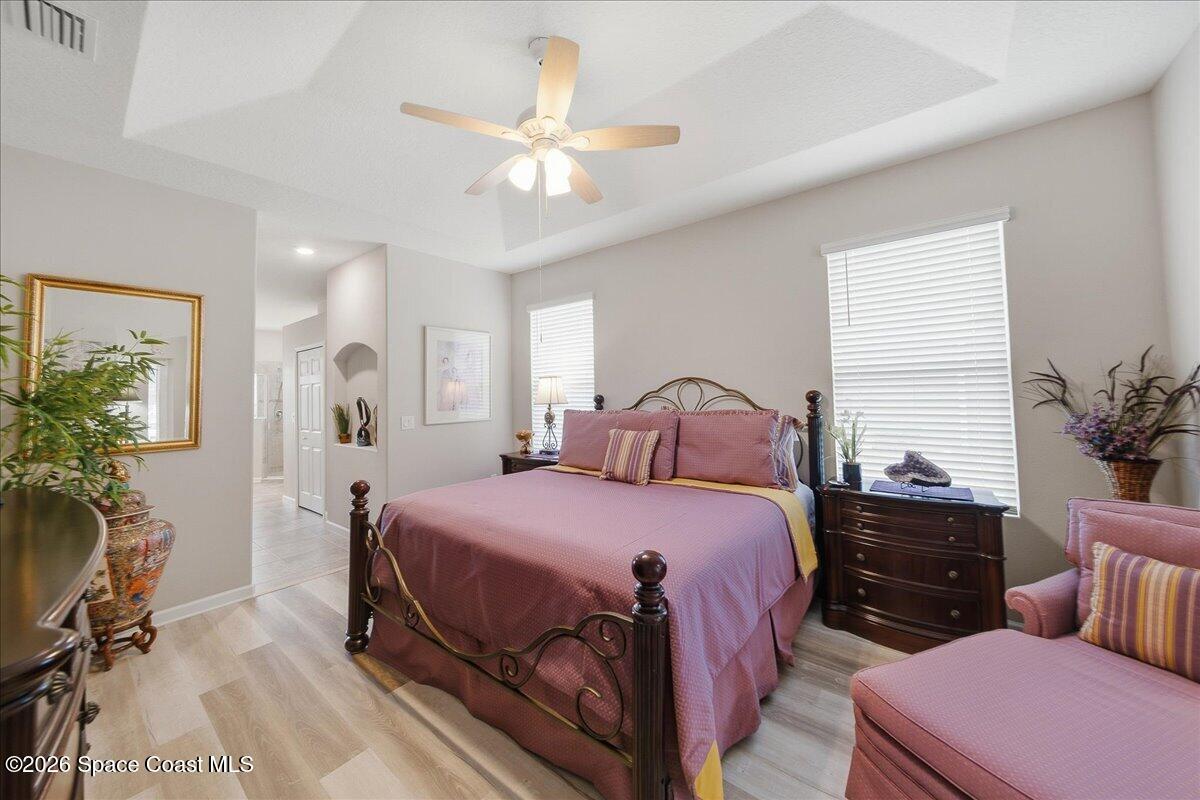 Furnished bedroom with a dark metal bed, pink bedding, matching seating, and a ceiling fan.