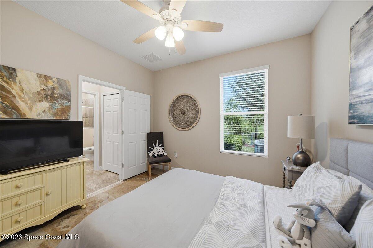 Bedroom with a large bed, ceiling fan, television, and window overlooking greenery.