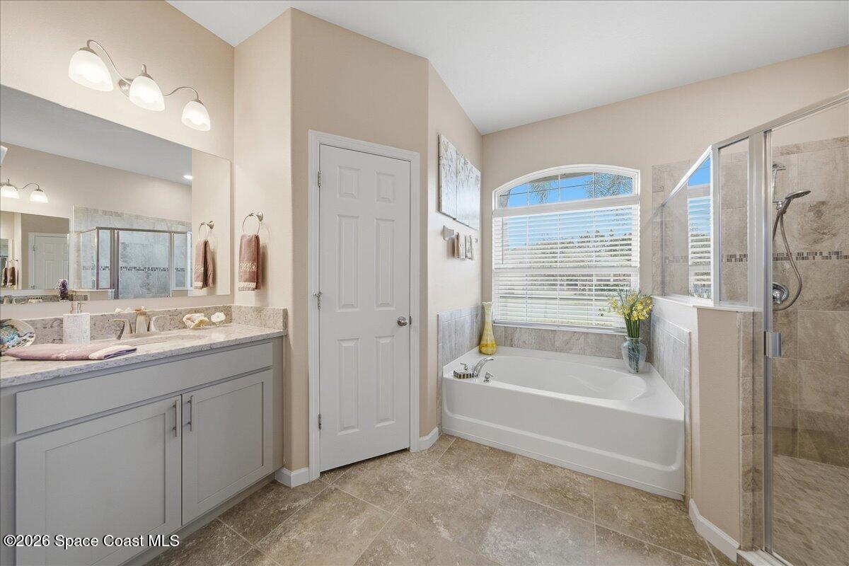 Primary bathroom with a gray double vanity, soaking tub beneath an arched window, and glass-enclosed shower.