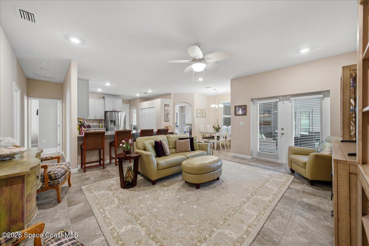 Open-plan living room with beige seating, tiled floors, and glass doors to a patio.