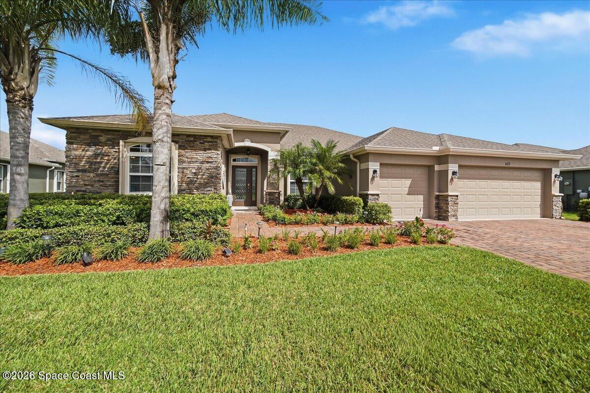 Single-story stone-front home with palm trees, landscaped beds, and a broad lawn.