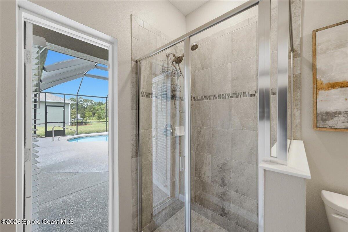 Bathroom with a glass-enclosed tiled shower and a view of the pool through the doorway.